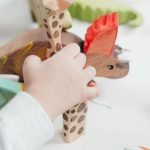 Childhood Education - Child Holding Brown and Green Wooden Animal Toys