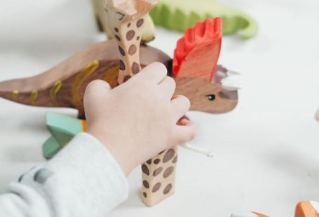 Childhood Education - Child Holding Brown and Green Wooden Animal Toys