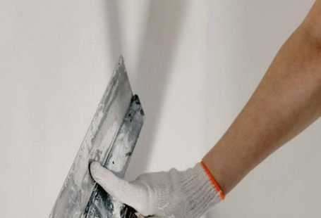 DIY Projects - Crop anonymous male worker in gloves holding putty knife while working at home